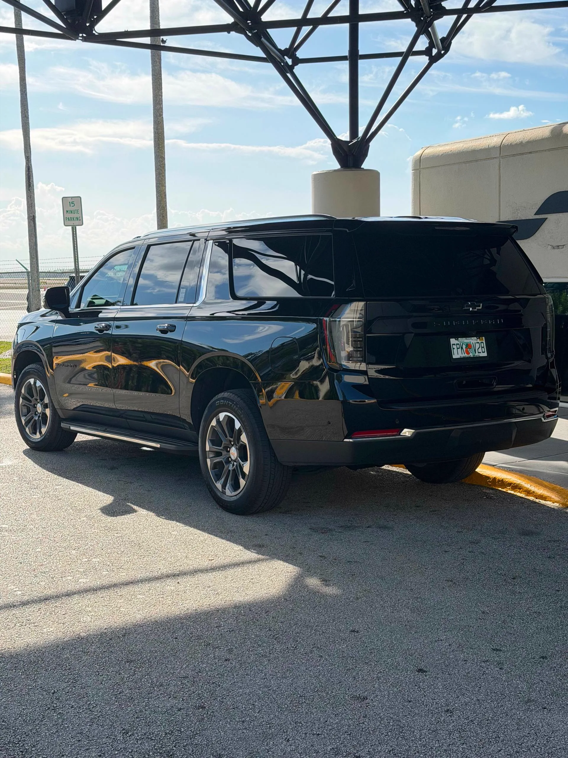 Black SUV waiting at an airport curbside under a canopy in daylight