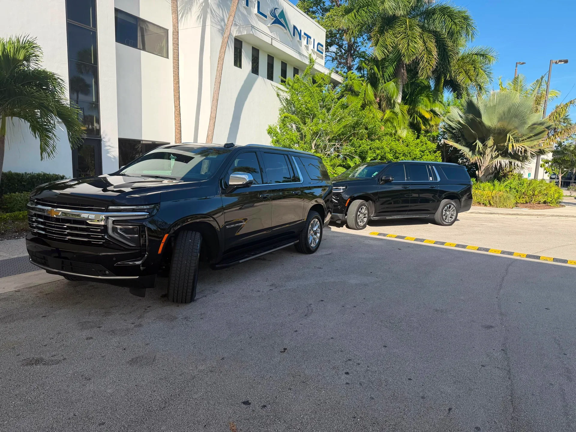 Black SUVs parked outside the Atlantic Aviation private terminal with palm trees around