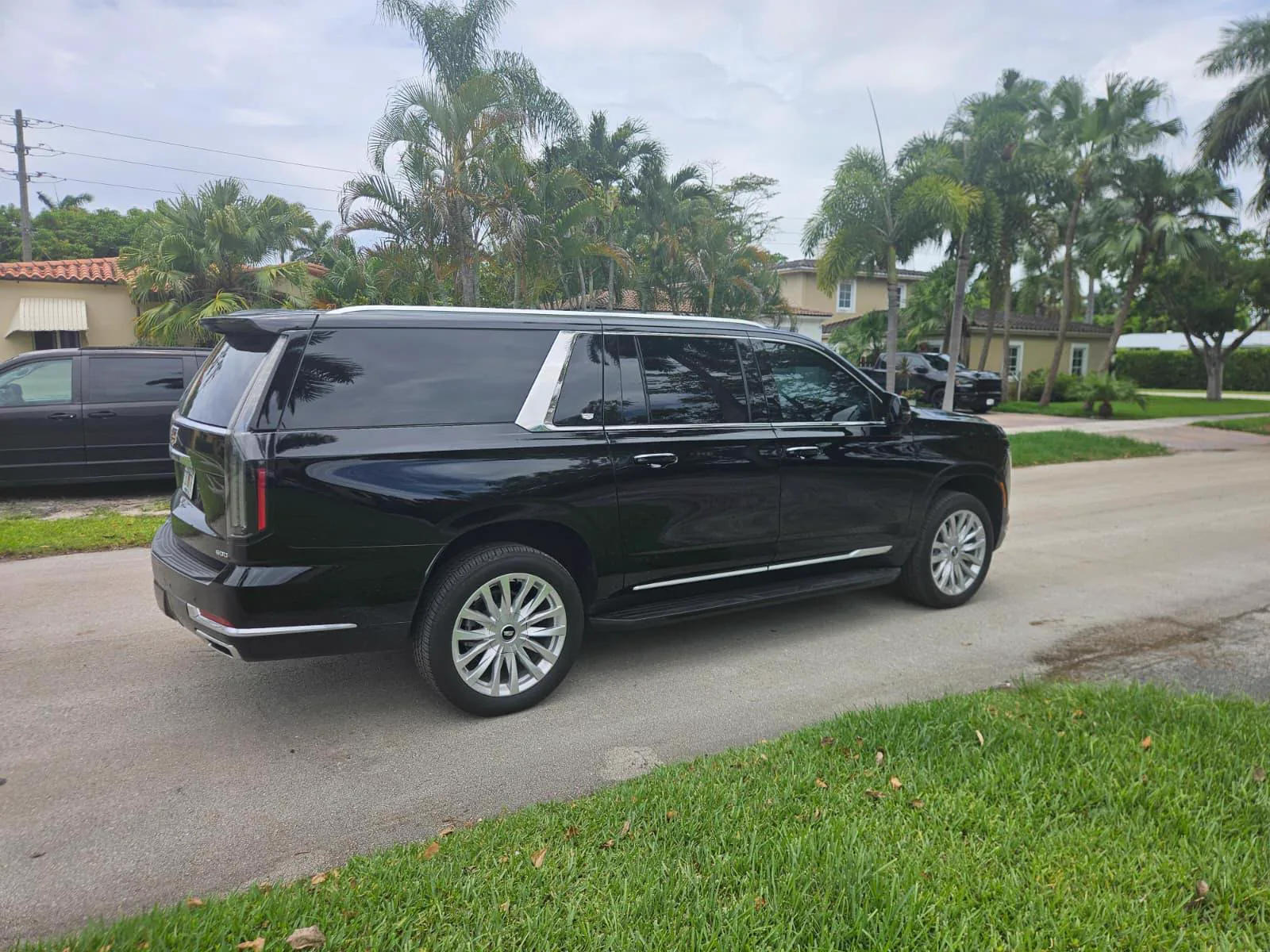 Rear three-quarter view of a black Cadillac Escalade parked among palm trees on a Miami street