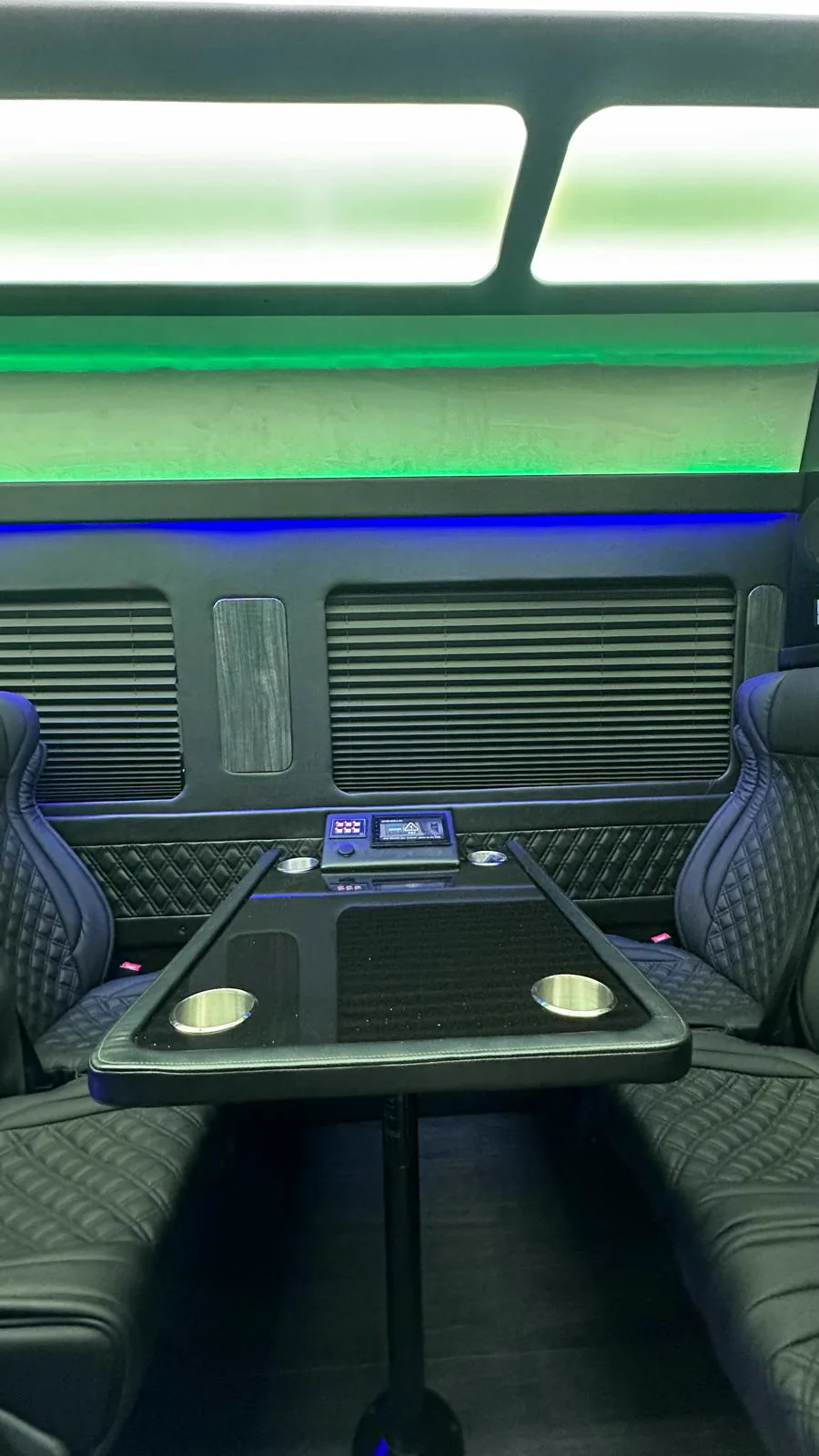 Asientos enfrentados alrededor de una mesa negra con portavasos bajo luz azul y verde