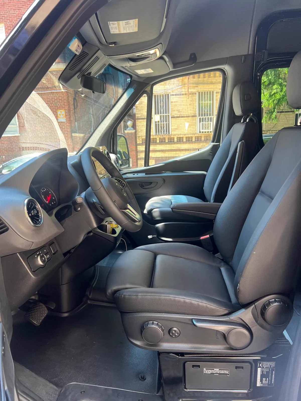 Driver area of a Mercedes-Benz Sprinter with the door open, steering wheel, instruments and black leather seats