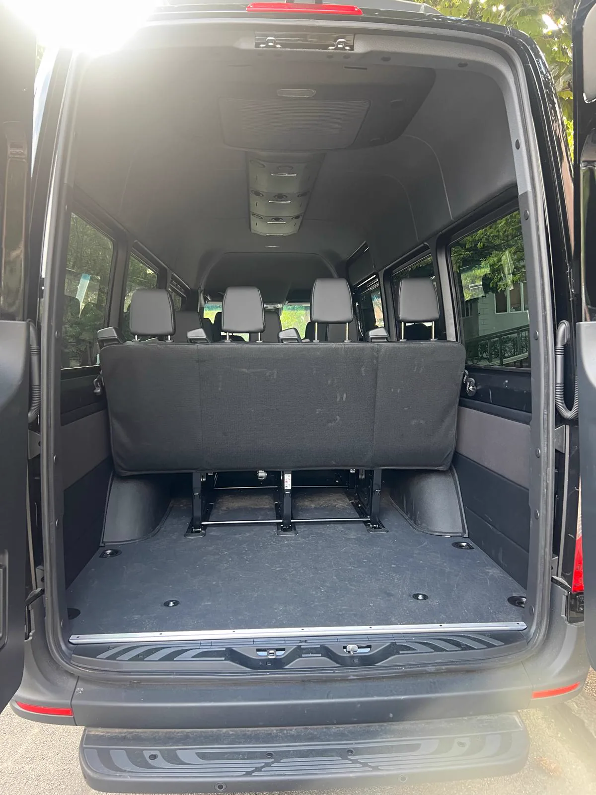 Rear doors open on a Mercedes-Benz Sprinter, showing the empty flat luggage floor and the rear bench seat
