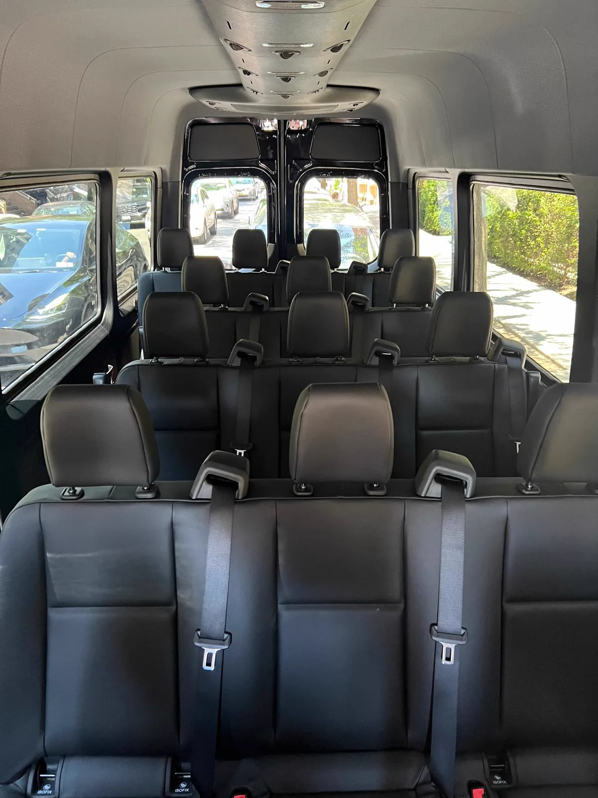Rows of black leather seats with headrests inside a high-roof Mercedes-Benz Sprinter, seen from the rear